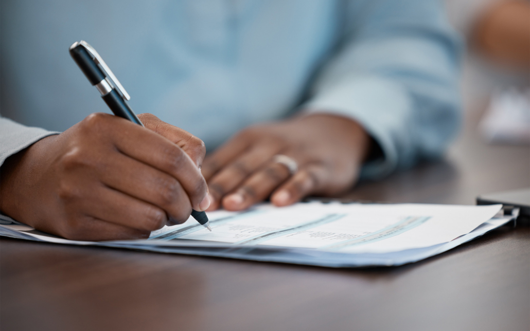 Hands Of A Man Signing Legal Paperwork At A Table Or Desk In The Office