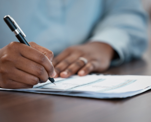 Hands Of A Man Signing Legal Paperwork At A Table Or Desk In The Office